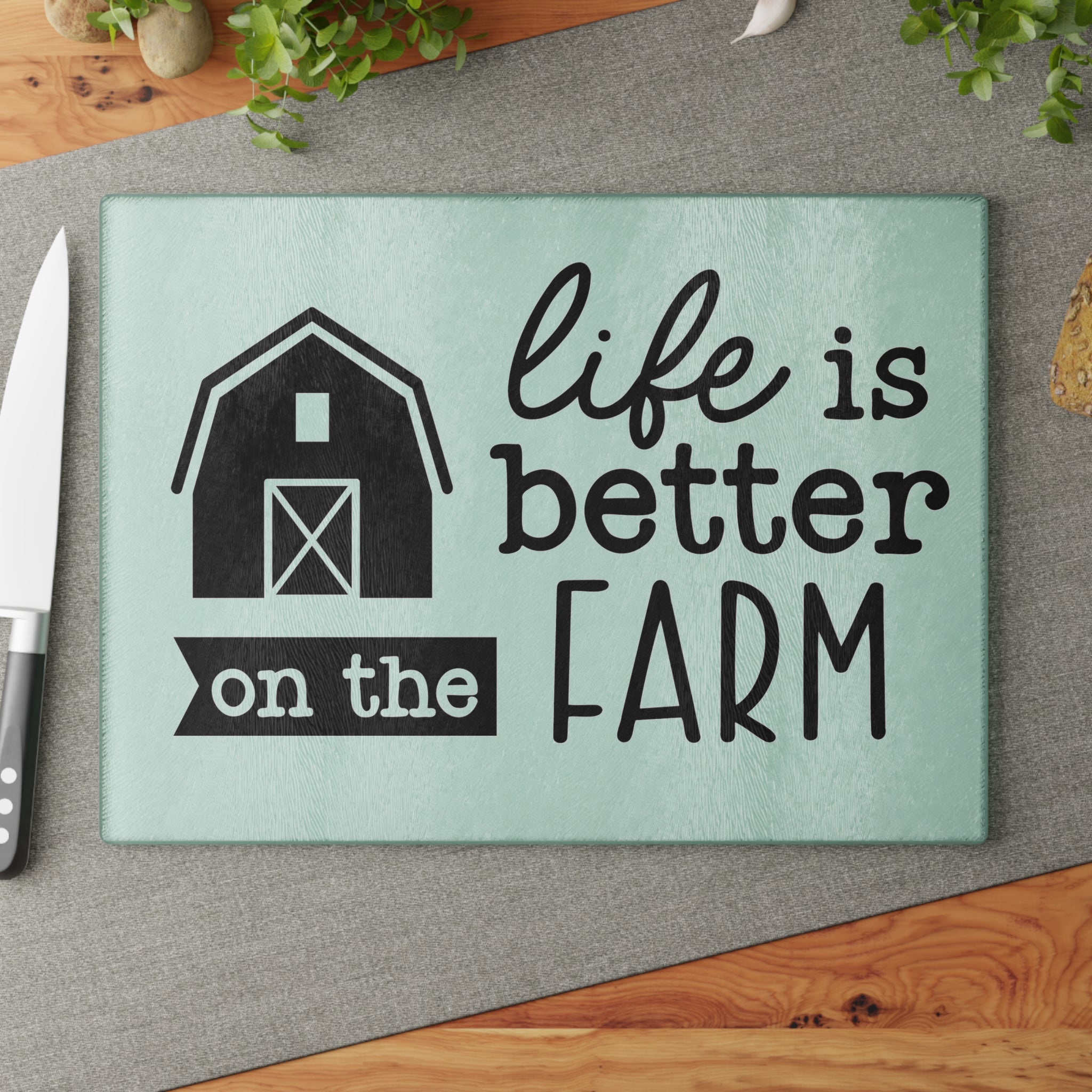 glass cutting board with the words "life is better on the farm" on a brown table with a gray runner and knive as decorwhite background