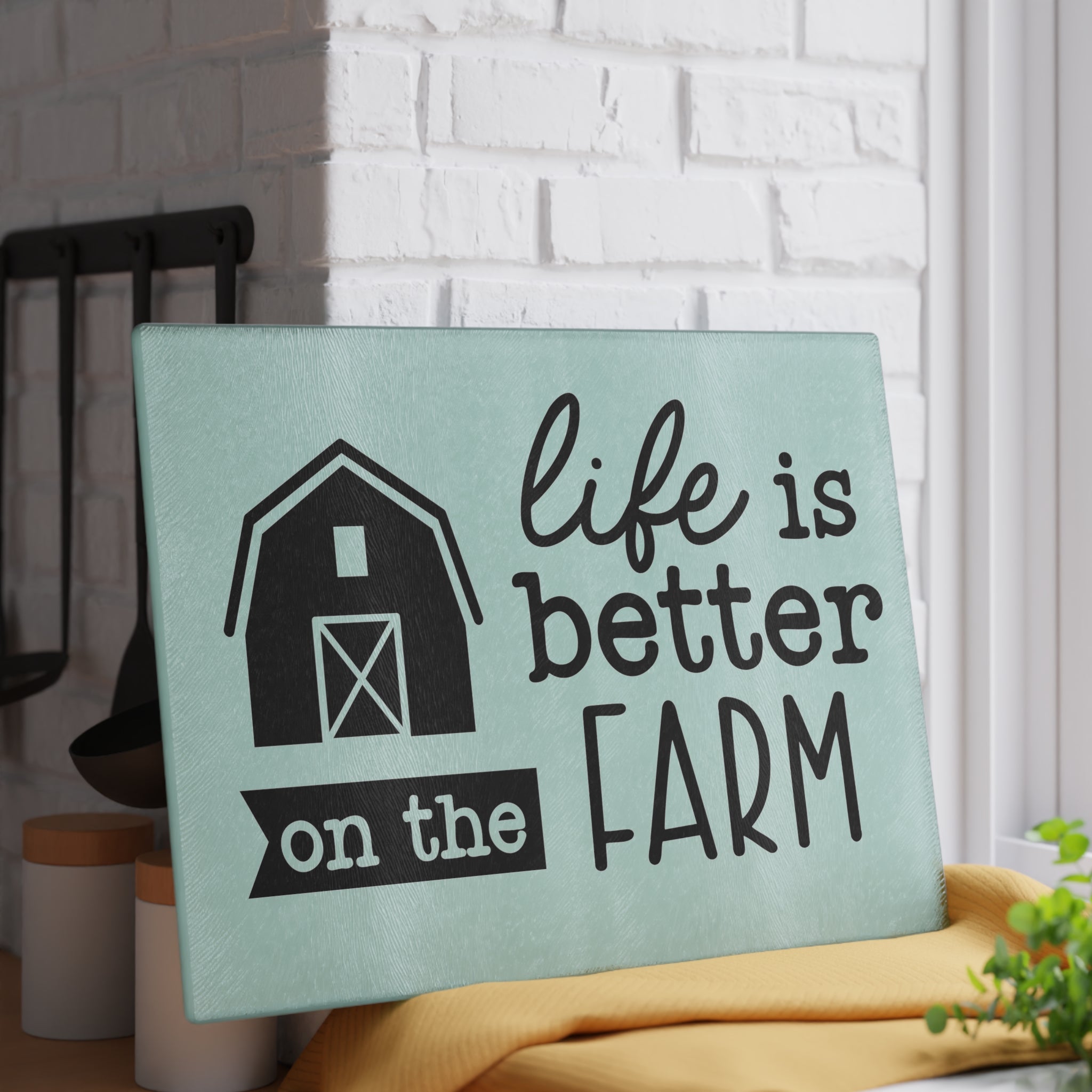 glass cutting board with the words "life is better on the farm" against a white brick wall
