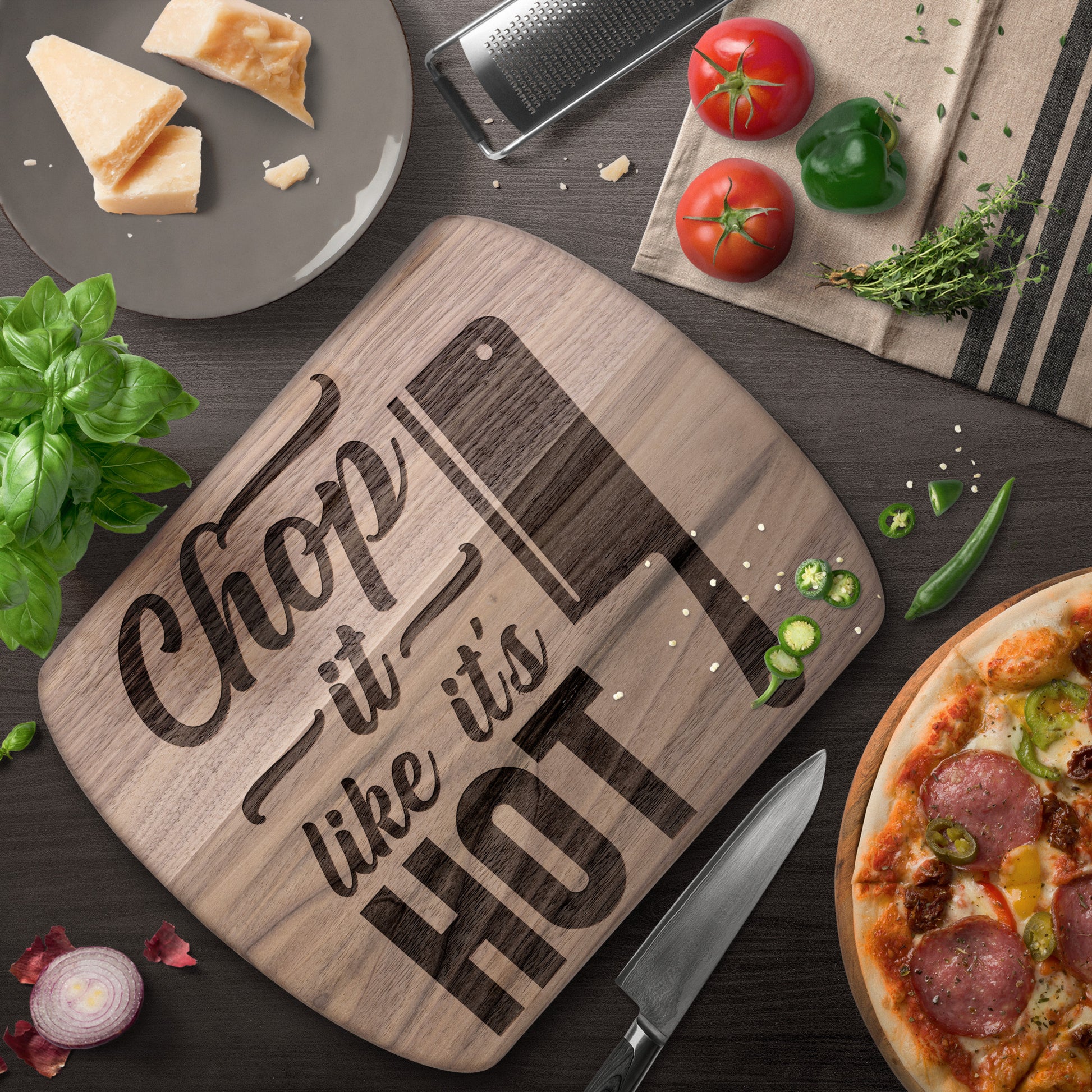 Walnut cutting board with words "chop it like it's hot" on brown table with a pizza and knife and decoration.