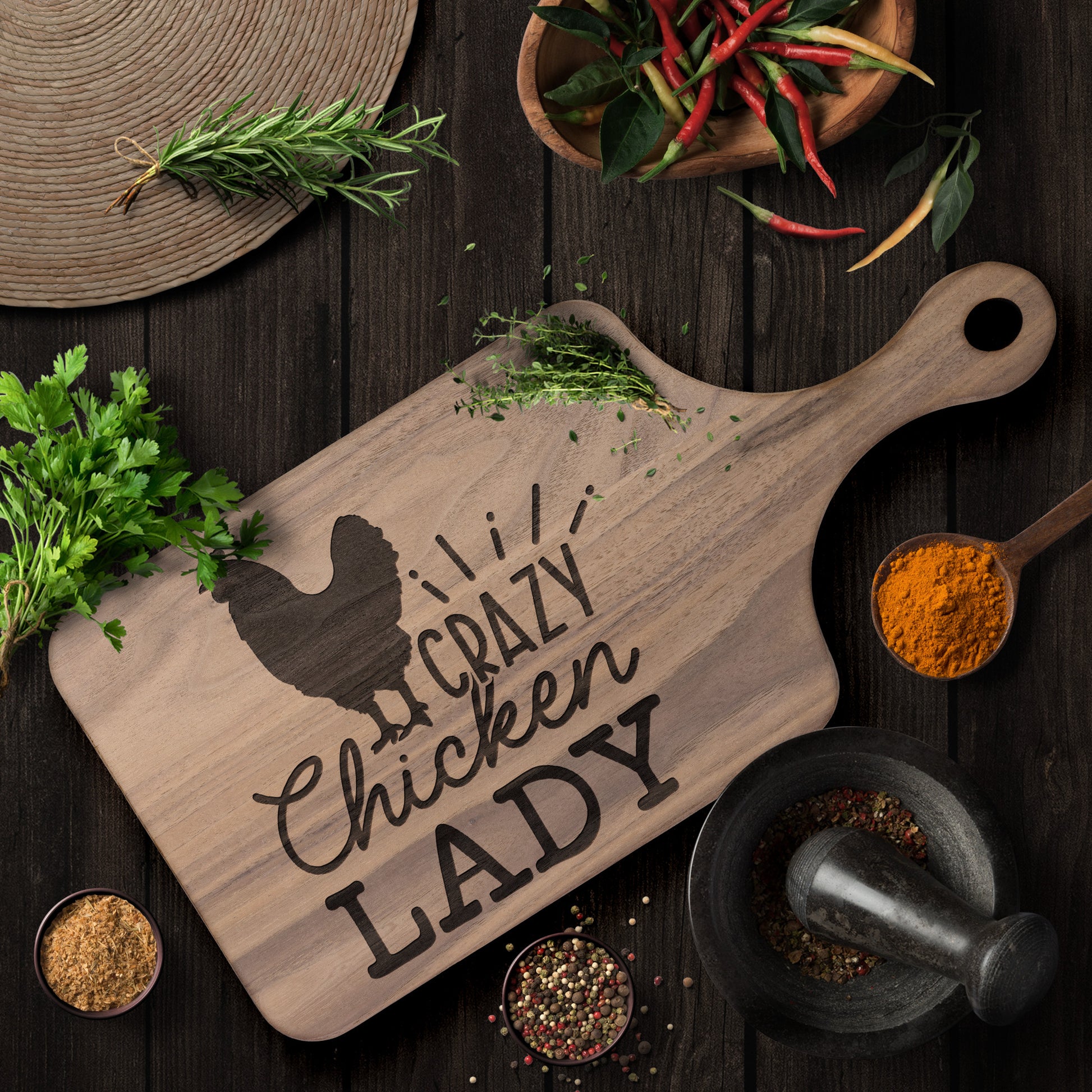 walnut cutting board with the words "crazy chicken lady" engraved on a brown table with herbs and spices as decor