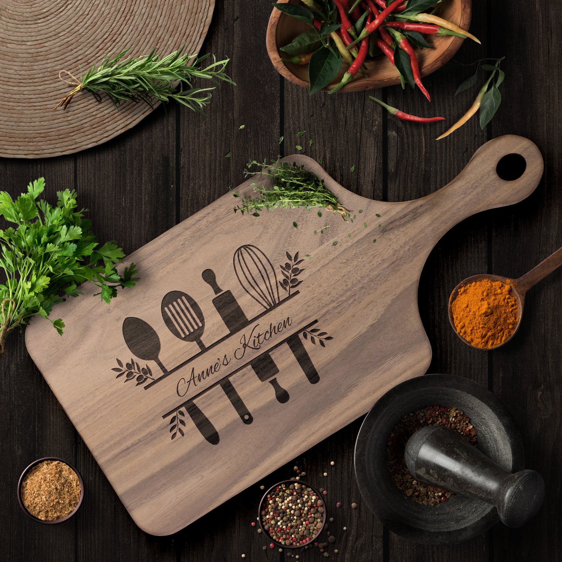 view of personalized walnut paddle cutting board on a dark brown table with herbs and spices as decoration