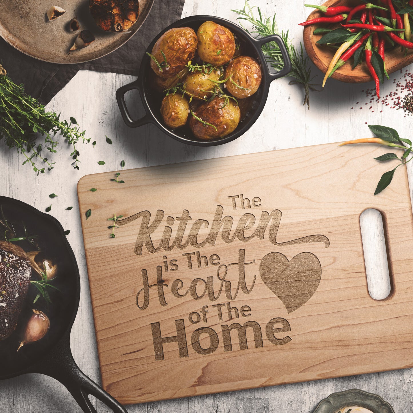 view of a maple cutting board with the words "The Kitchen is the Heart of the Home" on a white table with potatoes and spices as decoration